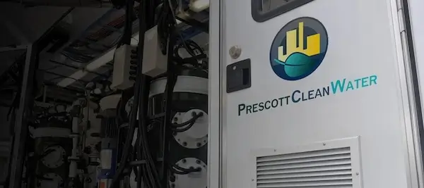 Door labeled 'Prescott Clean Water' with company logo, adjacent to complex water filtration equipment inside a facility