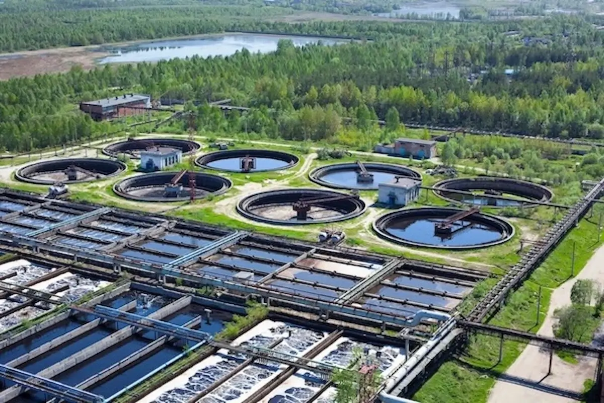 Aerial view of a water treatment facility with multiple circular and rectangular sedimentation tanks surrounded by greenery